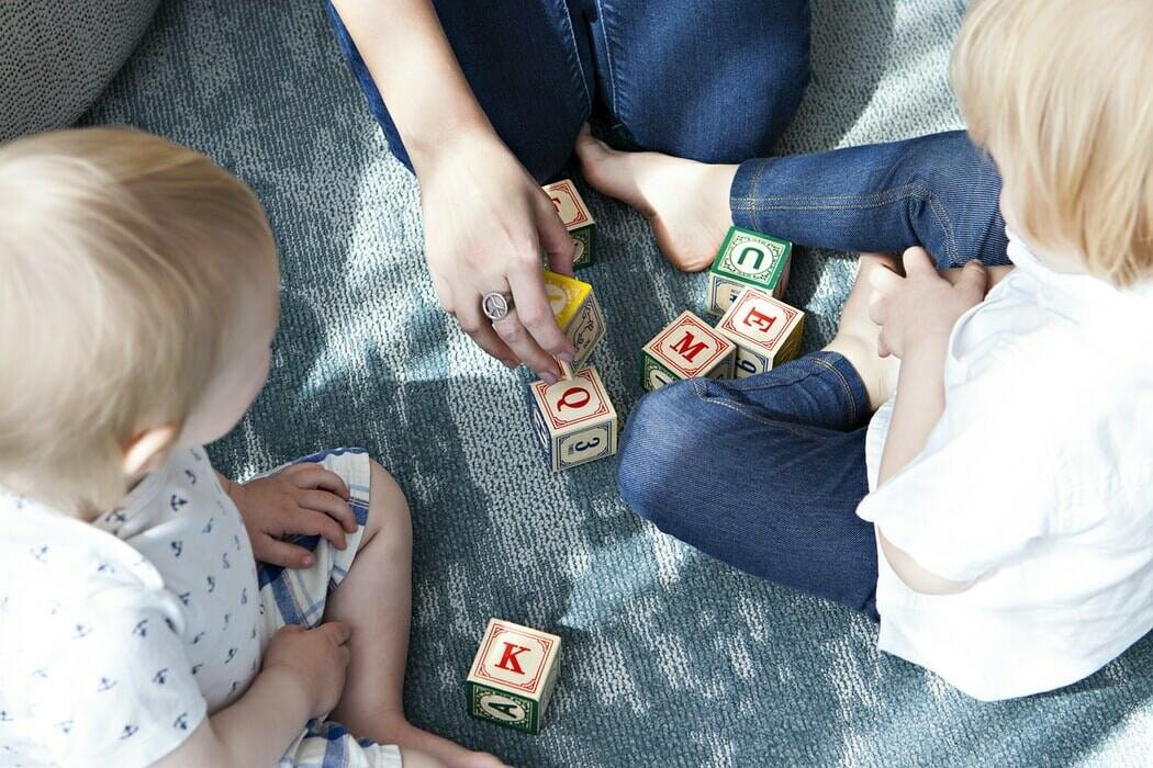 A mother sitting on the carpet teaching and playing with her kids with wooden blocks with letters