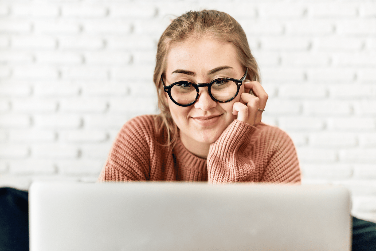 Smiling young woman wearing glasses while looking at her laptop screen