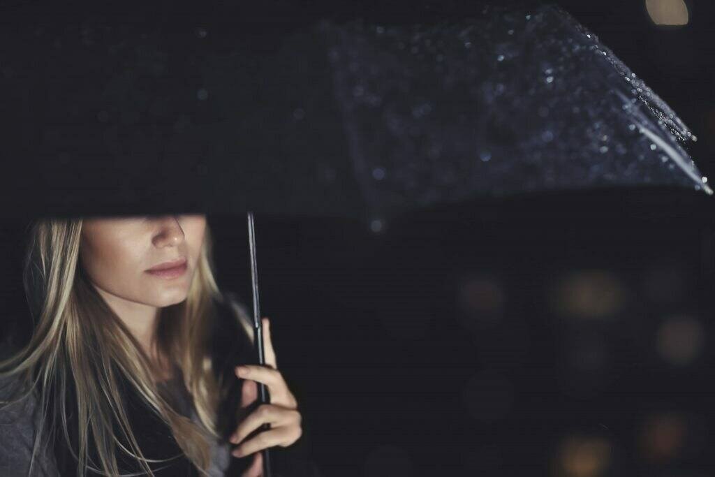 Half face woman under black umbrella on a rainy night