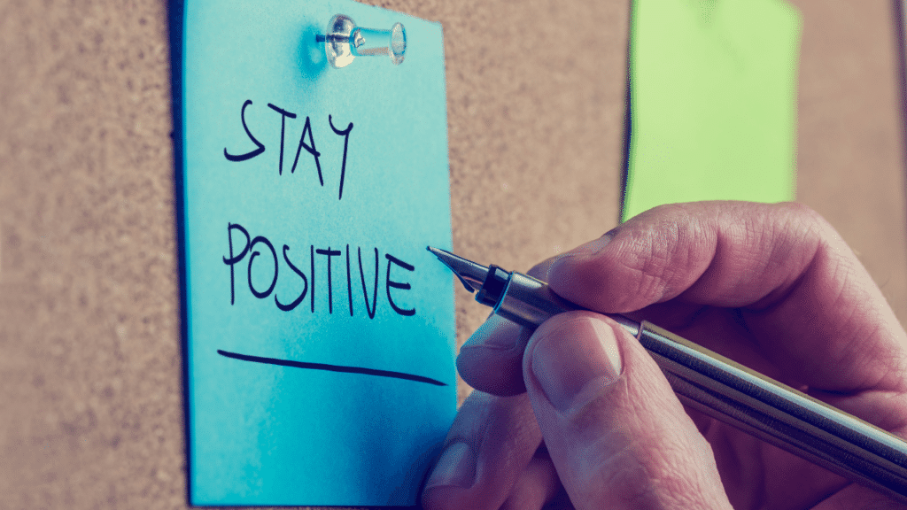 Writing the words "Stay Positive" on a note pinned on the bulletin board